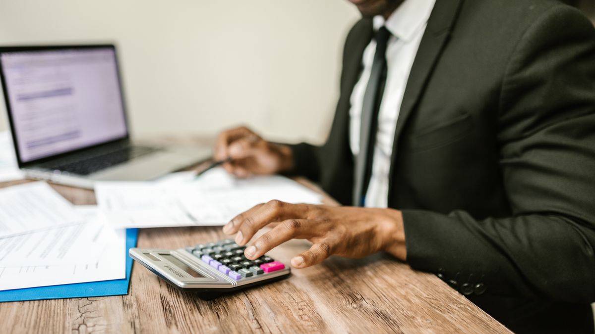 Profissional conferindo documentos com notebook e calculadora para consultar os dados de uma empresa
